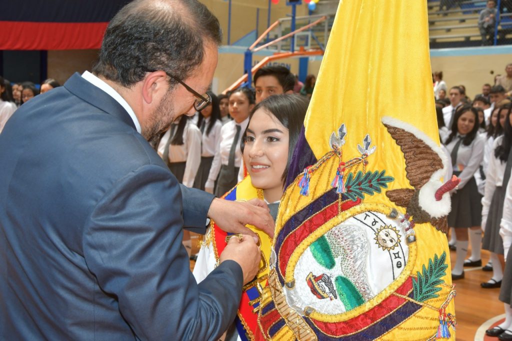 El rector del colegio, Alonso Guamán Castillo, entrega el Pabellón Nacional a María Augusta, en el marco de un acto solemne por el Día de la Bandera.