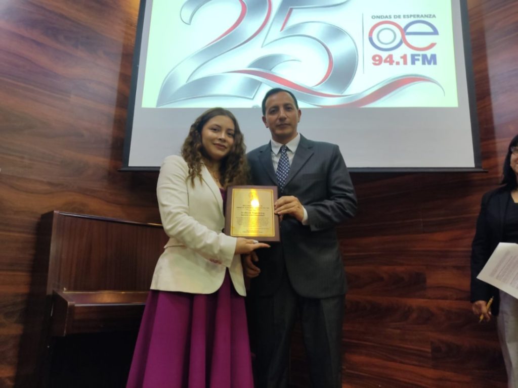 La profesional Andrea Sánchez entrega al director, Fabián Armijos, un reconocimiento por los 25 años de fundación de la radioemisora.